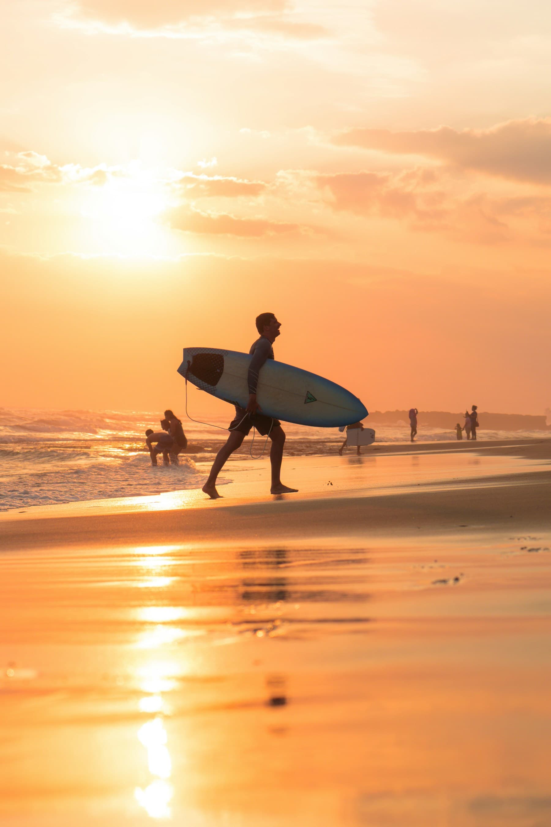 Un surfeur rejoint l’océan, sa planche sous le bras, dans la lumière du soir